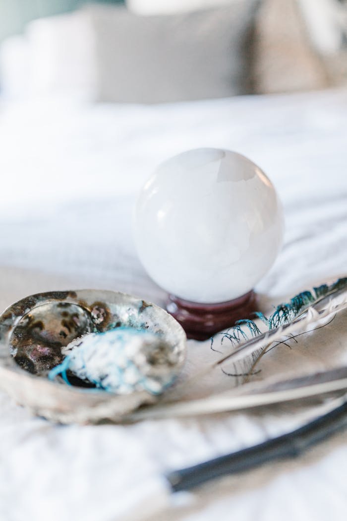contact-img Crystal ball and feather with smudging tools on a soft surface, ideal for spiritual and mystical themes.