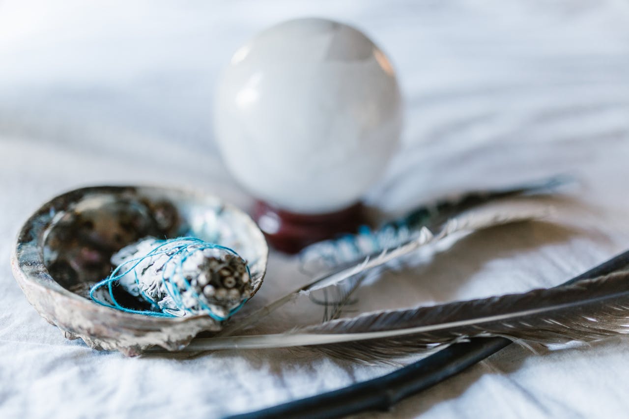 services-01 A spiritual arrangement featuring a crystal ball, sage bundle, and feathers, ideal for mystical themes.